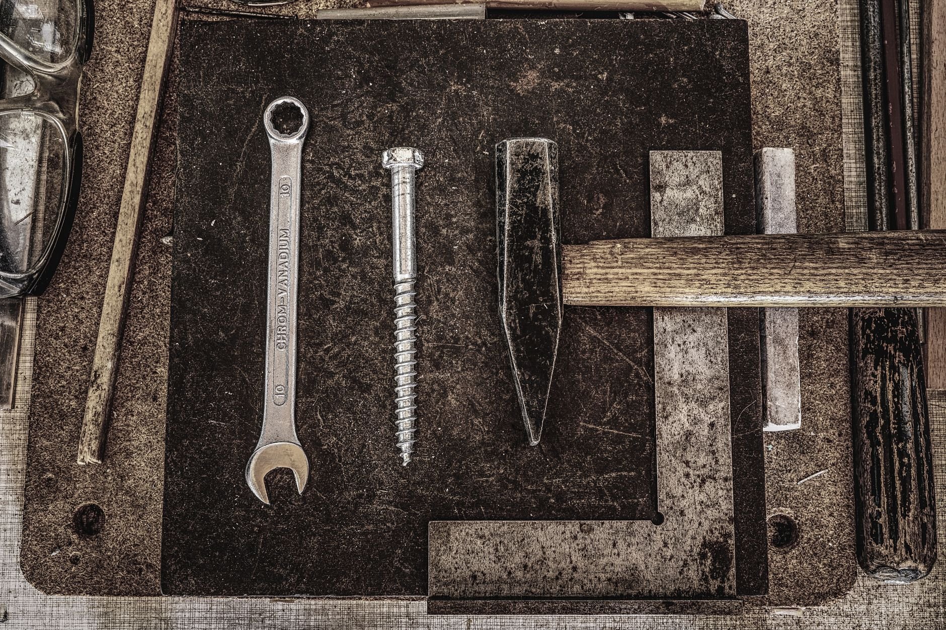 A collection of vintage workshop tools including a wrench, nail, and hammer displayed on a wooden table.